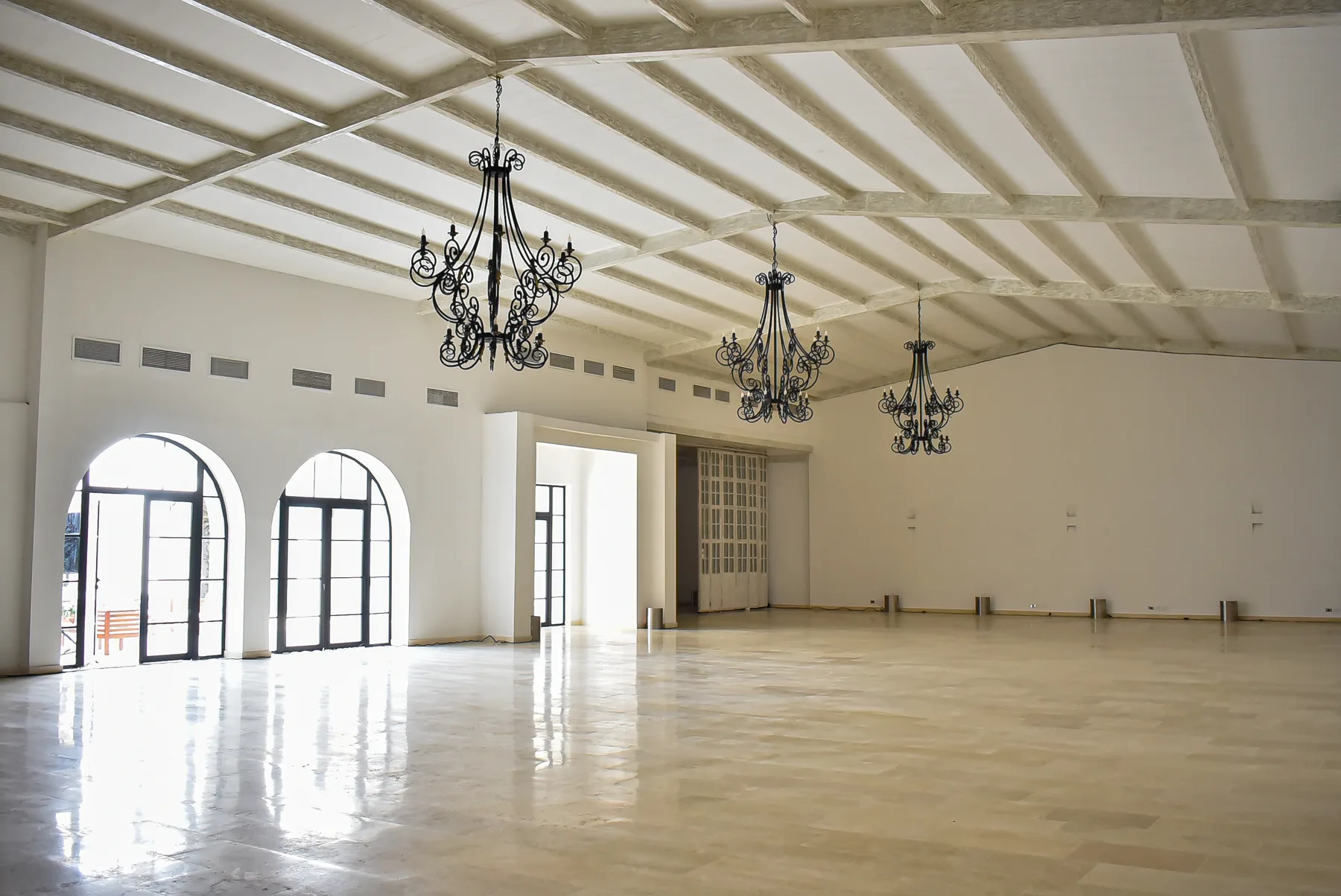 Salón vacío de Casa Real con puertas arqueadas y lámparas ornamentales